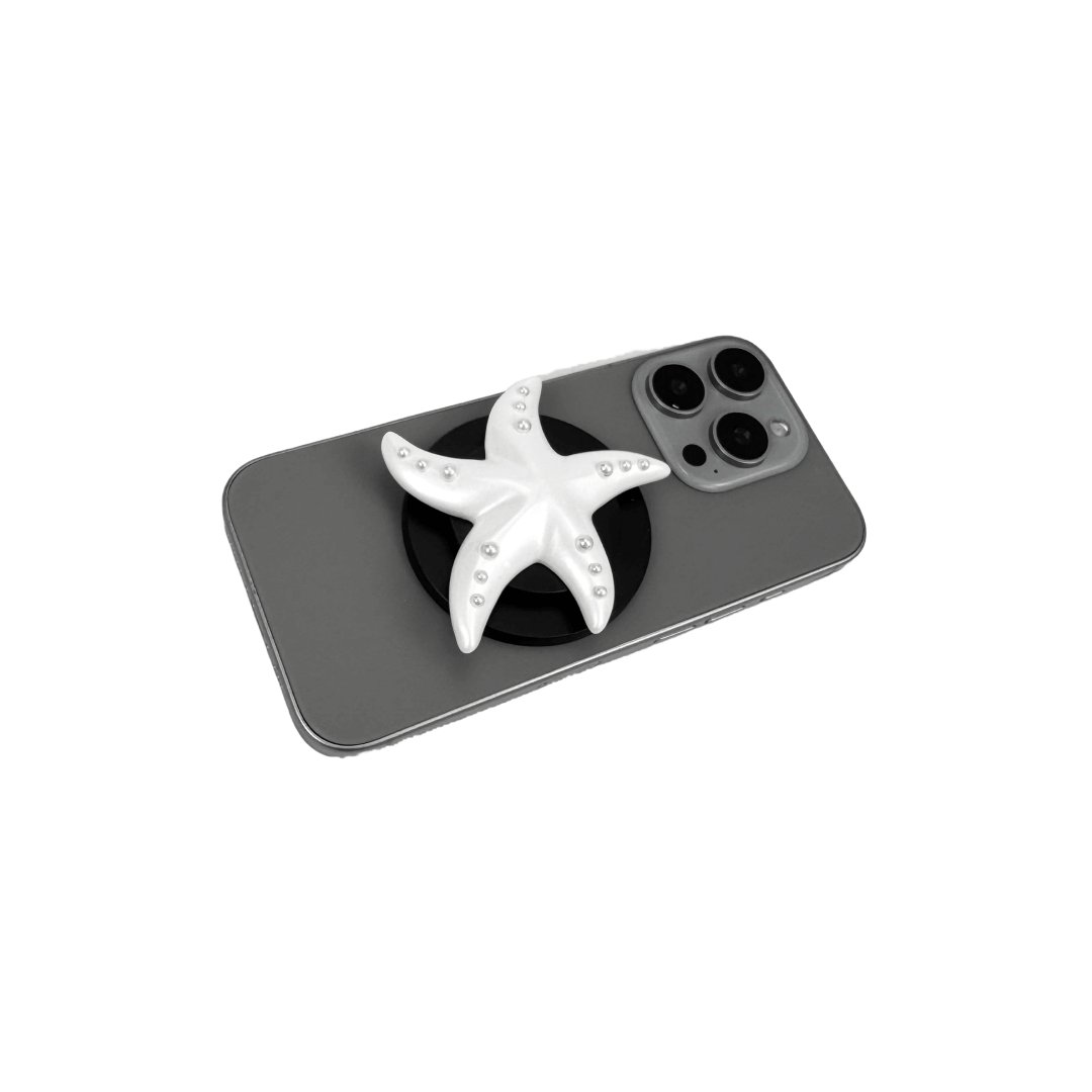 Glossy white, silver, gold and pink starfish-shaped phone grip with embedded rhinestones, mounted on a black base and attached to a gray iPhone case. 