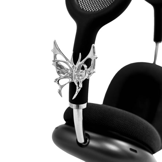 Chrome thorned butterfly-shaped accessory clipped onto AirPods Max.