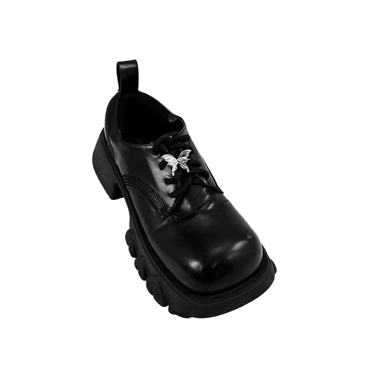 Chrome butterfly shoe accessory clipped onto the laces or vamp of a black sneaker or leather shoe.
