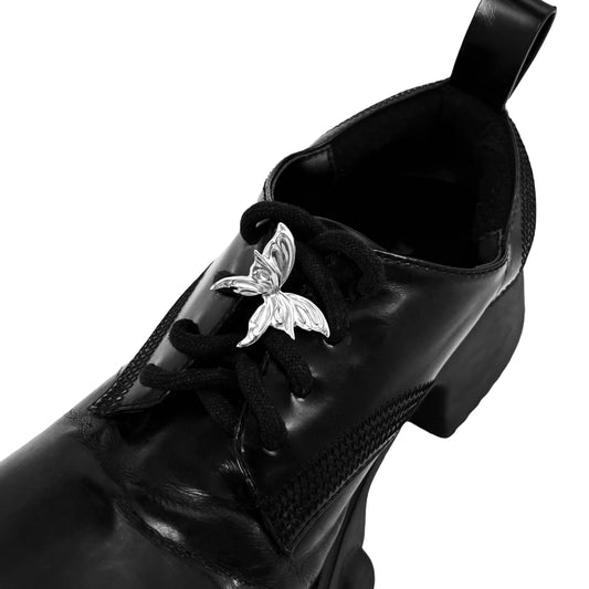 Chrome butterfly shoe accessory clipped onto the laces or vamp of a black sneaker or leather shoe.